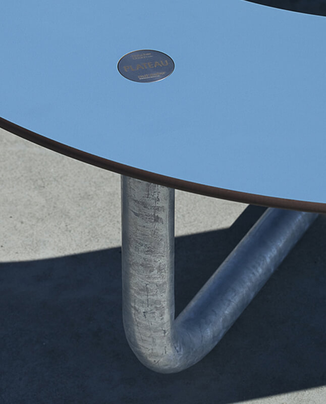 Nærbillede af et blåt PLATEAU Picnic O bordbænkesæt udendørs, der viser kompaktlaminat og stål materialerne i detaljer
