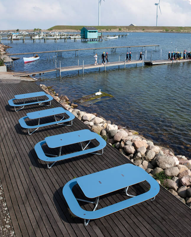 Fire blå PLATEAU Picnic O bordbænkesæt er placeret i en række med udsigt til havnen