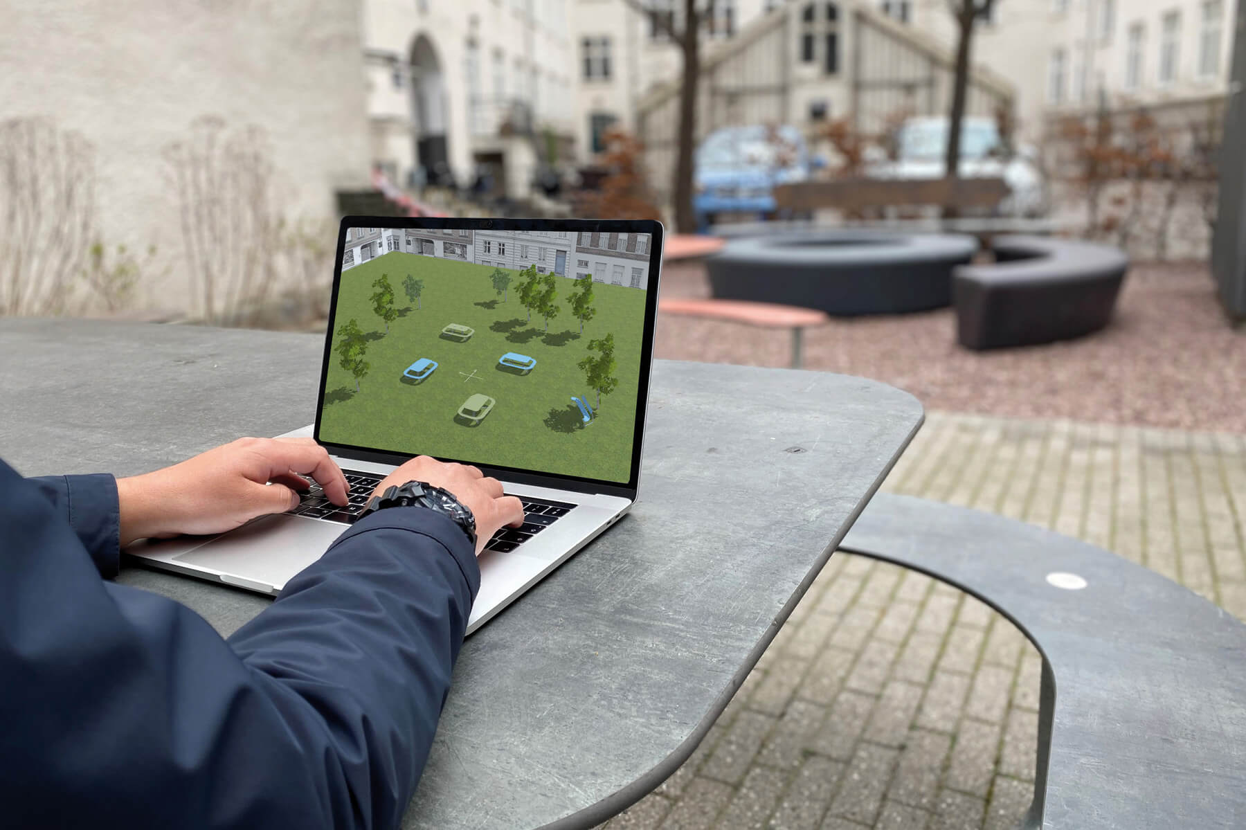En mand sidder udendørs på en bænk med en computer foran sig. Han demonstrerer brugen af ViZu 3D-værktøjet på computeren