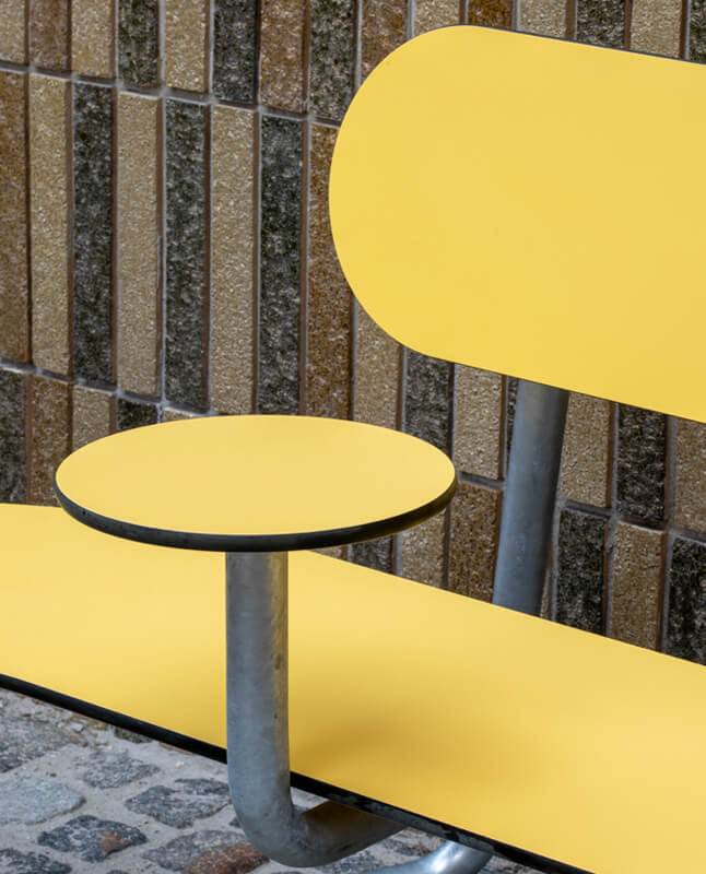 Et nærbillede af en gul Plateau Bænk med armlæn