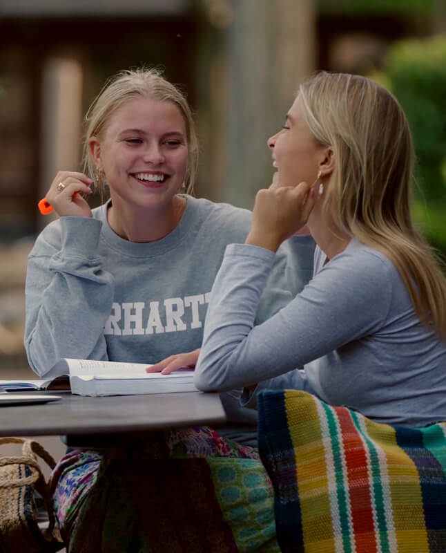 To glade piger sidder på et picnicbord udendørs og deler latter sammen