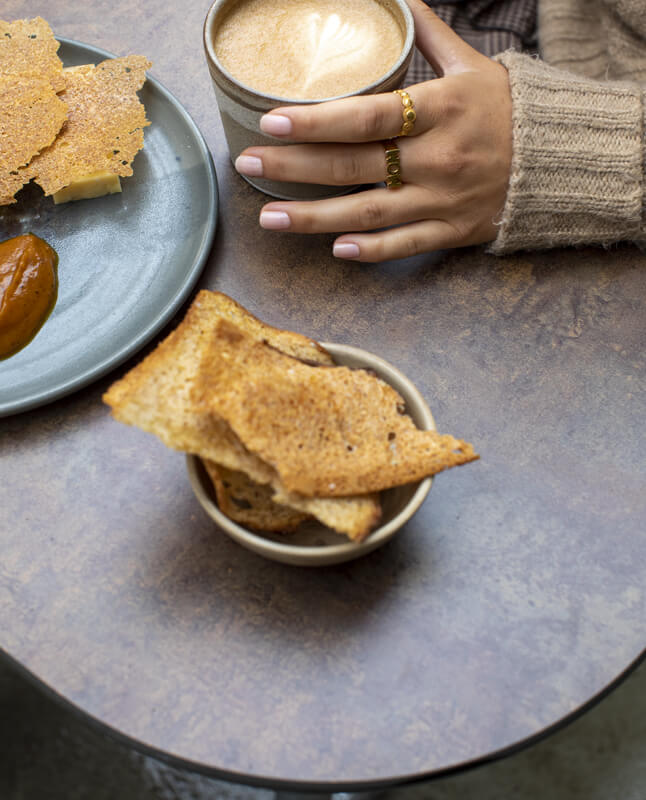 Et nærbillede af et brunt Plateau Picnic Duo bordbænkesæt, hvor man kan se mad og en kvindes hånd holde en kop kaffe