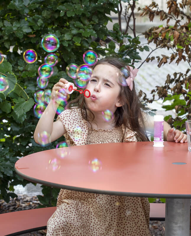 En pige der puster sæbebobler ved et Plateau Picnic Round bordbænkesæt