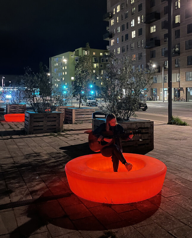En kvinde, der spiller guitar på en lysende Loop Light bænk i Ørestaden
