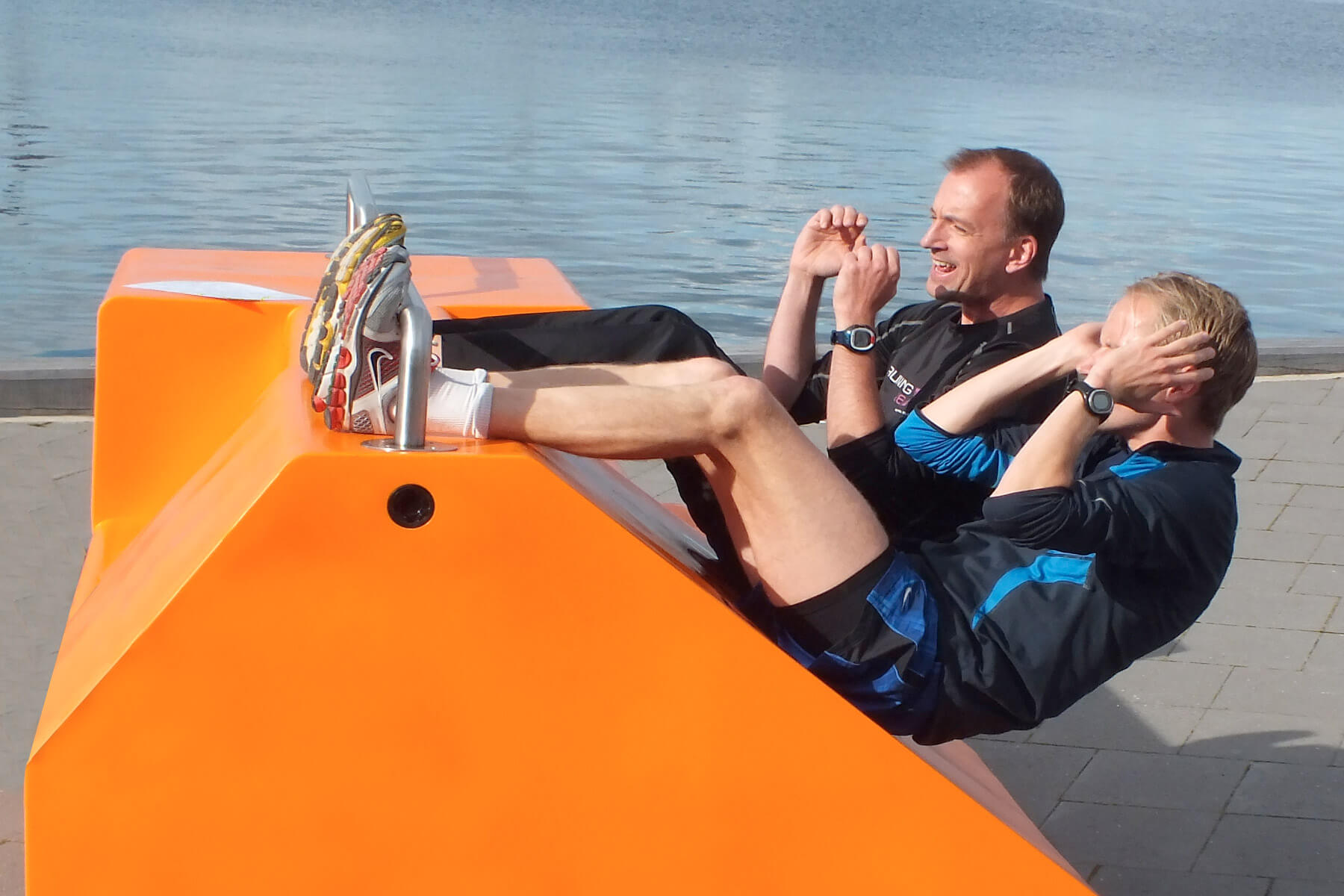 To mænd der træner på en orange FitStation i byrummet