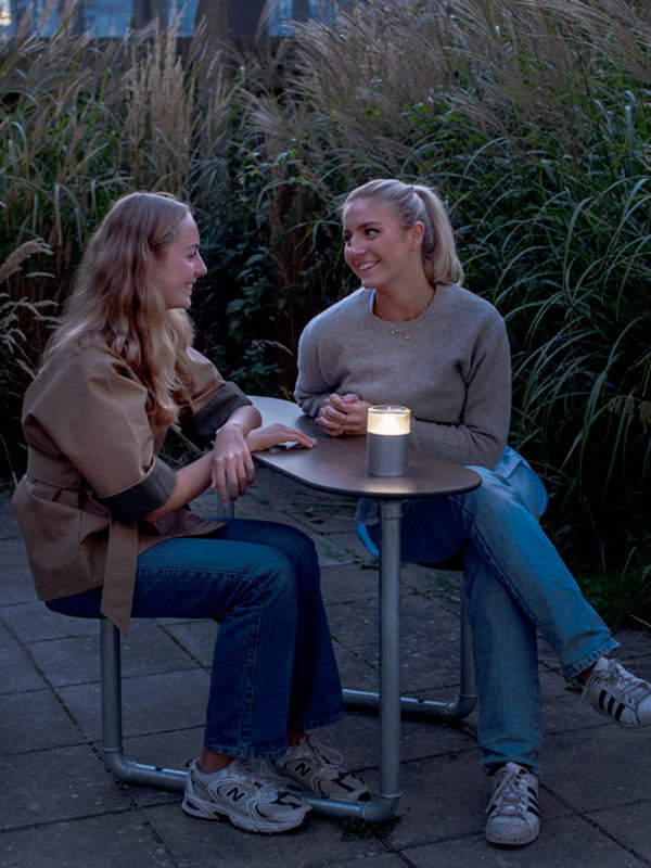 To kvinder ude i en gård, de sidder på Plateau Picnic Duo belyst med Plateau Point Sun