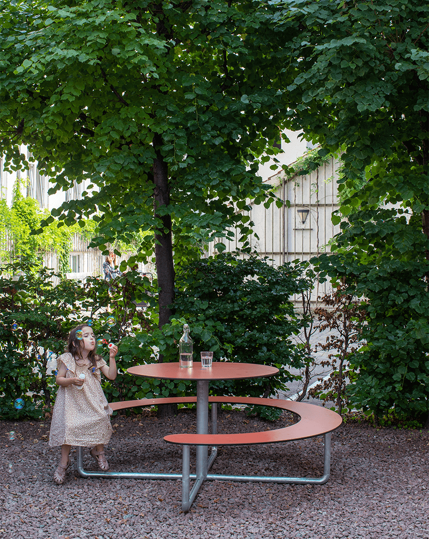En pige ved et Plateau Picnic Round bordbænkesæt i en gård, hun puster sæbebobler