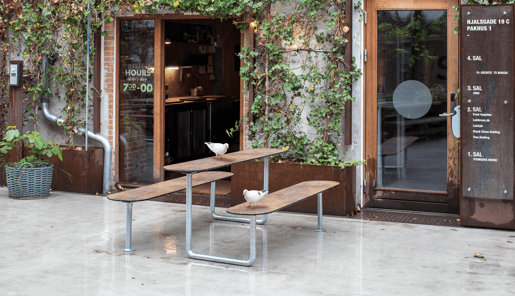 En due på et brunt Plateau Picnic Street bordbænkesæt ude foran en cafe i regnvejr